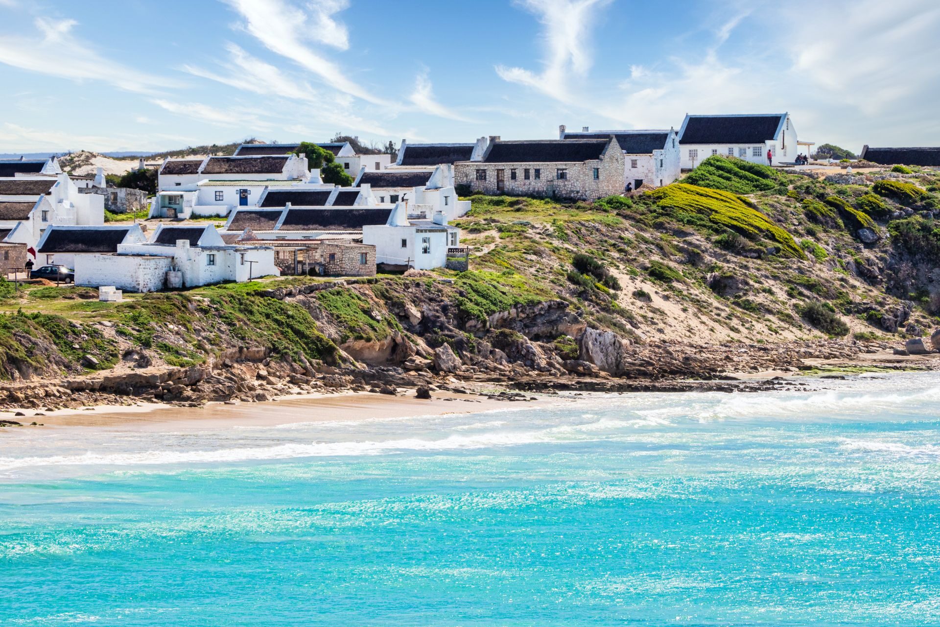 White holiday cottages on a green hillside above a turquoise beach