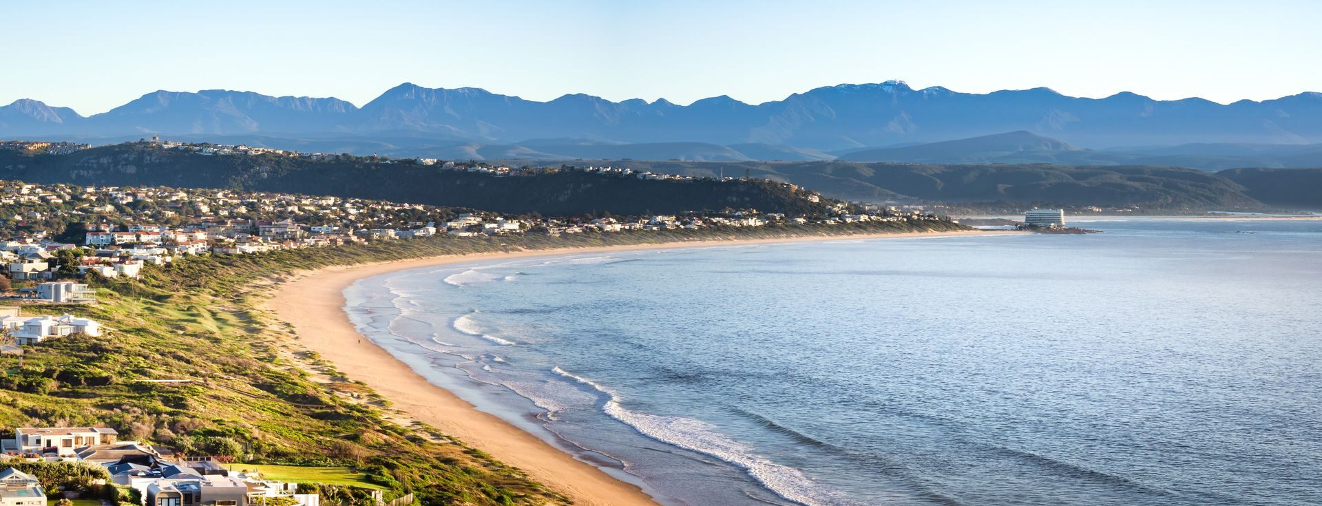 A wide golden beach curving toward blue mountains on the Cape Whale Coast